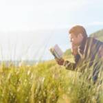 man reading a book in a grassy field