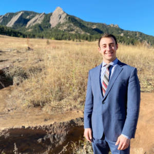 Young man in suit stands in front of mountains