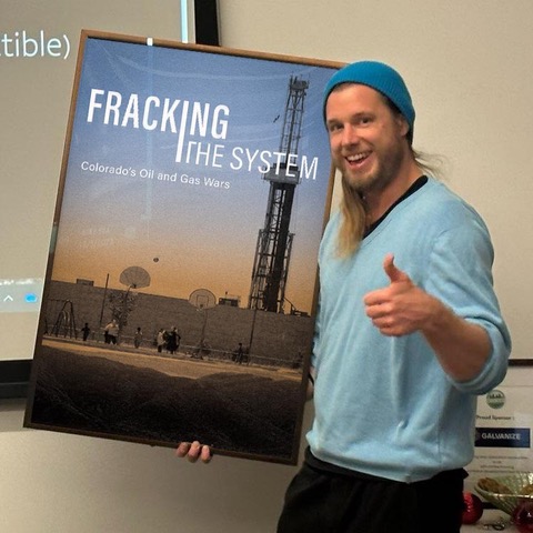 Brian gives a thumbs up holding a Fracking the System film poster