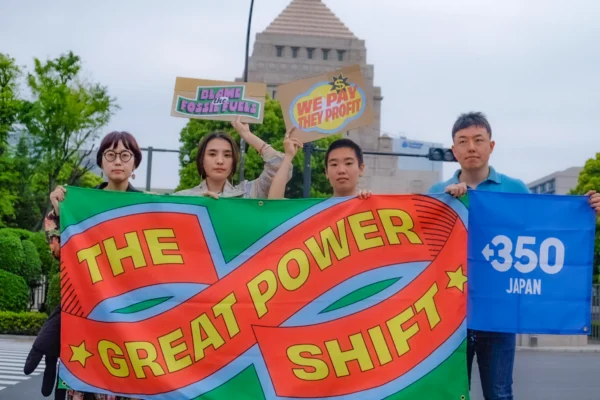 国会議事堂を拝啓に、「THE GREAT POWER SHIGT」とカラフルな文字で書かれた布バナーを掲げたアクティビストが4人並んでいる