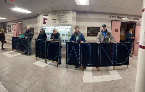 Half a dozen individuals hold lighted panels that spell out "Yes to Wind" in the lobby of a school.