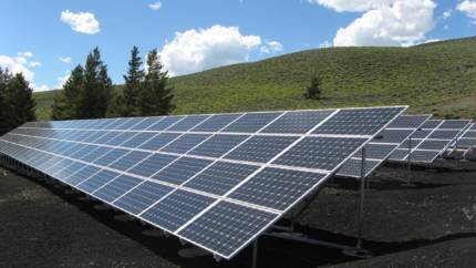 Two solar panels in front of a green hill under a blue sky.